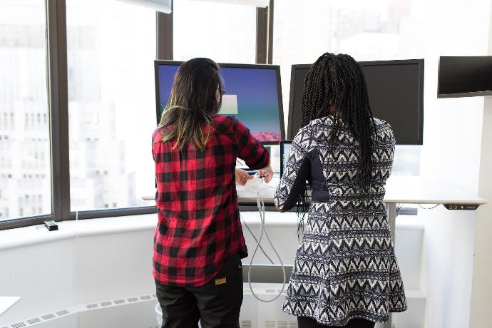 two women standing in front of two black monitors